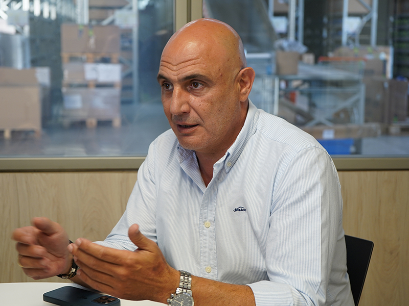 Hombre calvo con camisa blanca gesticulando con las manos mientras habla en una mesa en un entorno de oficina.