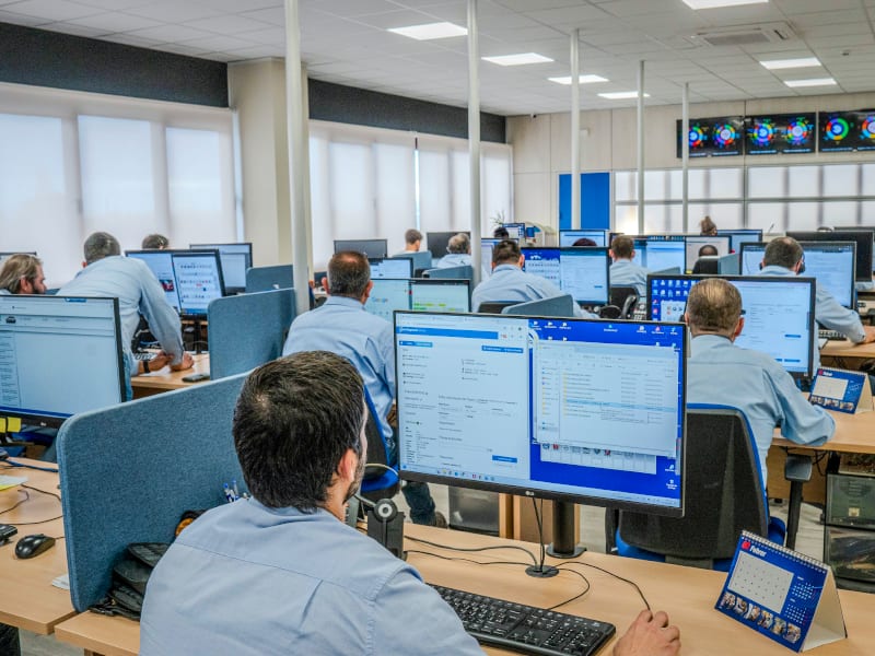 Oficinistas con camisas azules se sientan en mesas con monitores de ordenador en un espacio de oficinas luminoso y moderno, donde cada profesional del taller aporta su valor para ayudar al equipo a crecer.