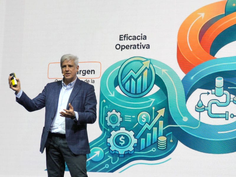 Hombre trajeado dando una presentación con coloridos gráficos de eficiencia y finanzas desplegados detrás de él.