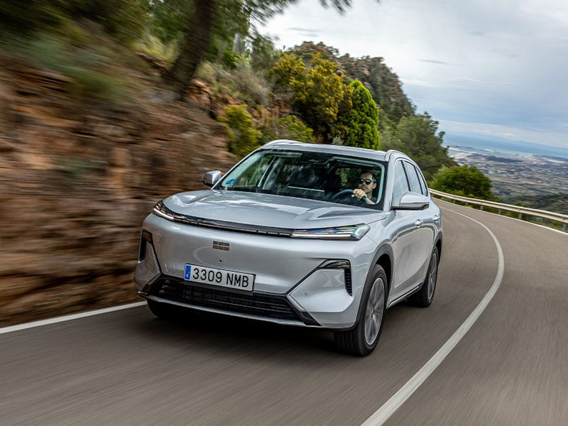 Un todoterreno enchufable Geely Starray EM-i híbrido plateado circula por una sinuosa carretera de montaña con un hombre al volante.