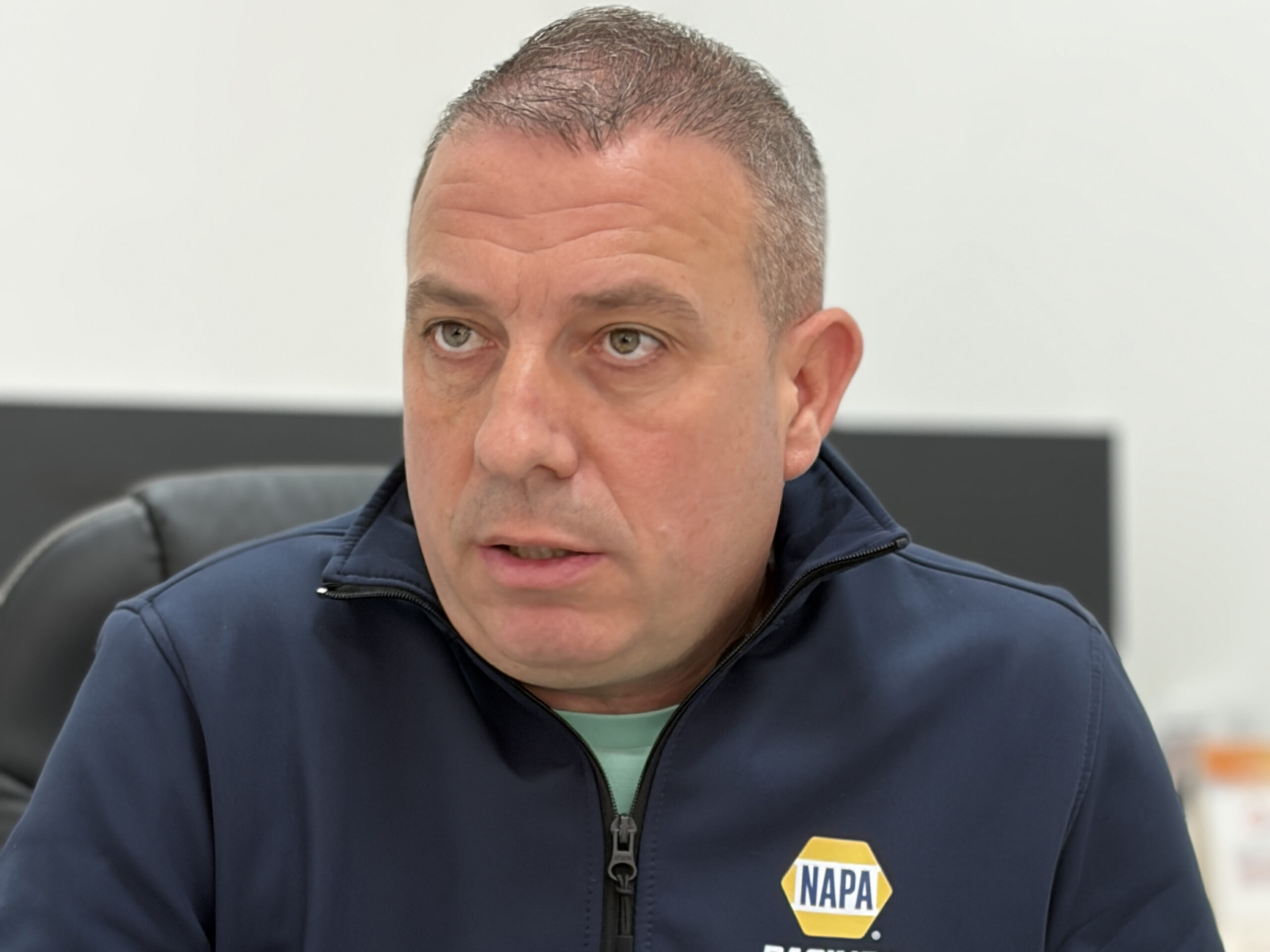 Un hombre con una chaqueta azul marino de NAPA está sentado en el interior, mirando ligeramente hacia un lado con expresión seria.