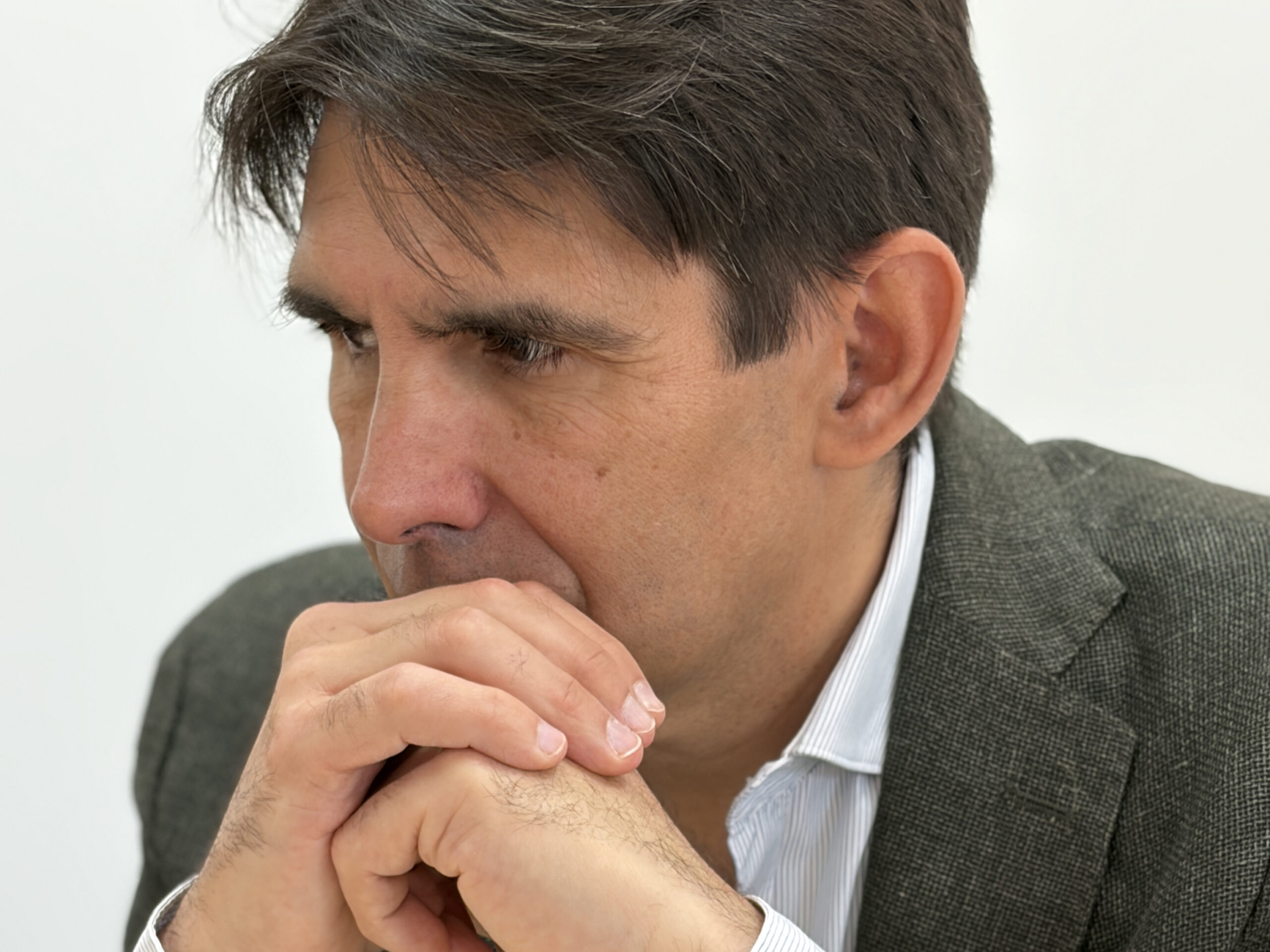 Hombre trajeado sentado con las manos juntas cerca de la boca, parece sumido en sus pensamientos.