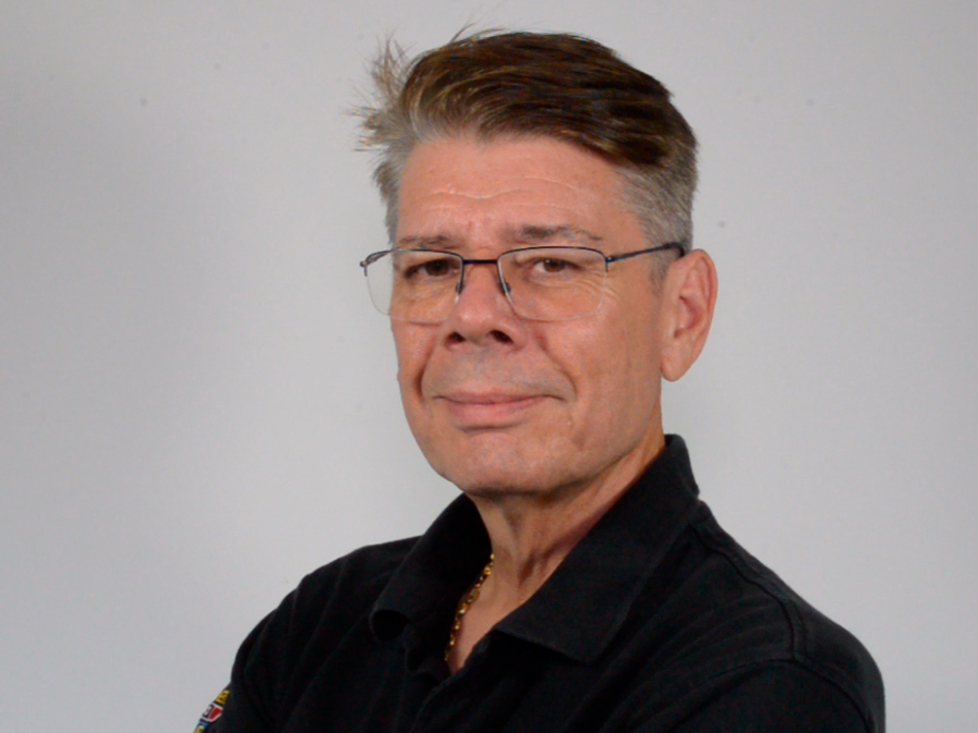 Hombre de mediana edad con pelo castaño corto, gafas y camisa negra, sonríe ligeramente sobre un fondo liso, lo que refleja confianza en el mercado y experiencia en posventa de frenado.