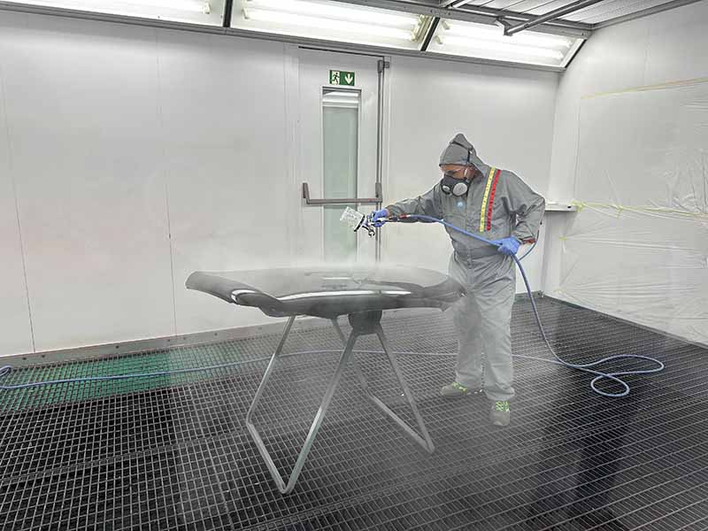 Una persona equipada con ropa de protección utiliza el sistema de mezcla Mix’n Shake para preparar el barniz PPG D8178 antes de pintar con pistola una pieza de coche en un espacio de trabajo cerrado y ventilado.