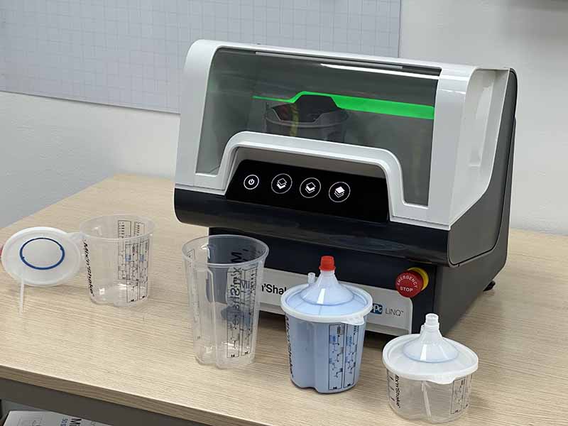 Una batidora de laboratorio colocada sobre una mesa, con vasos medidores y recipientes con líquido azul delante, en la que se muestra el sistema de mezcla Mix’n Shake para aumentar la productividad de PPG.