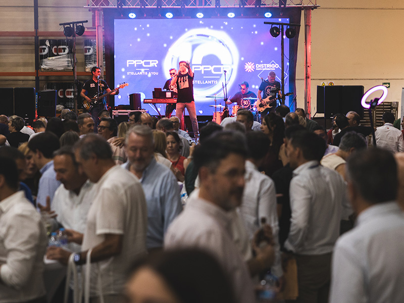 Una banda actúa en el escenario de un evento celebrado en un recinto cerrado en España, con motivo de su décimo aniversario, ante una gran multitud y con una pantalla al fondo.