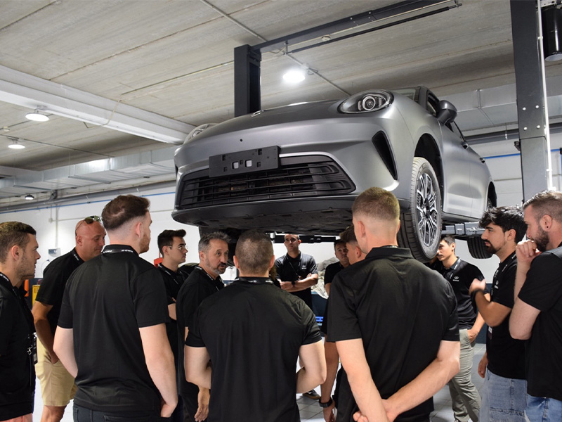 Un grupo de personas se encuentra reunido alrededor de un coche GWM elevado sobre una plataforma en un garaje cubierto o un taller, hablando sobre los servicios posventa.