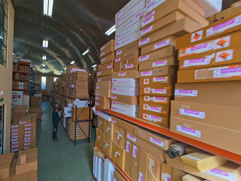 Una persona está de pie en un almacén lleno de cajas de cartón apiladas y estanterías.