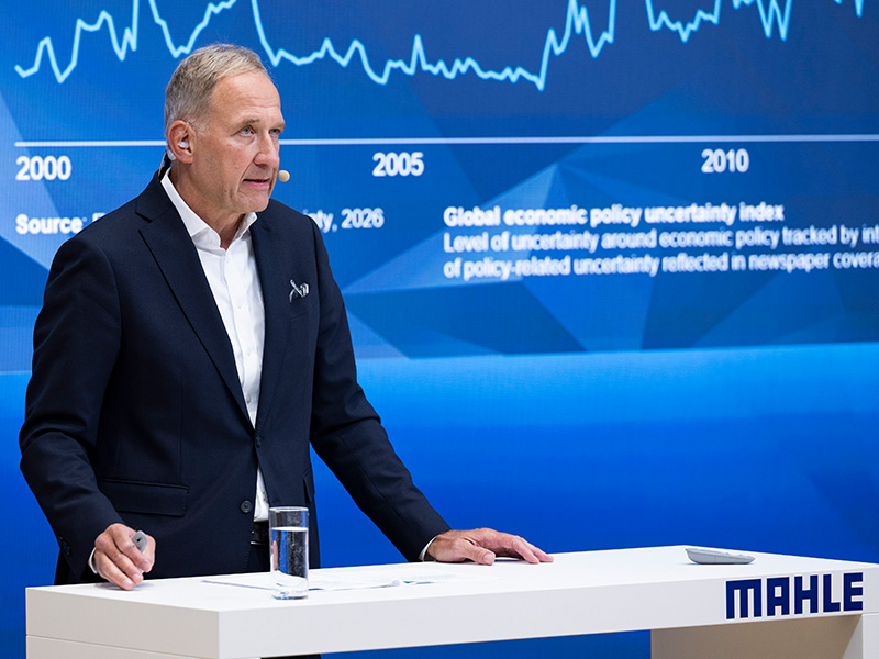 Un hombre vestido con traje habla desde un atril con el logotipo de «MAHLE» y, a sus espaldas, se muestran un gráfico y datos económicos, en los que se destaca el papel cada vez más importante del hidrógeno en Europa y su creciente relevancia para la Península Ibérica.