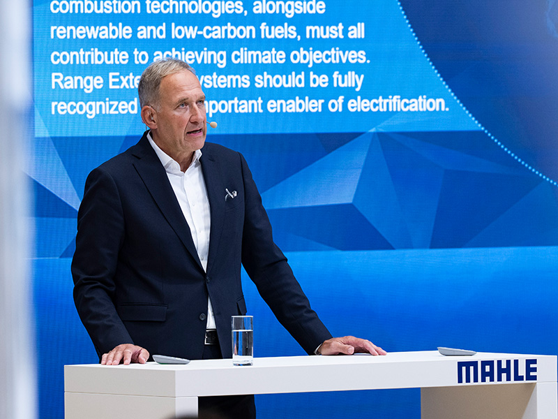 Un hombre vestido con traje habla desde un atril con el logotipo de «MAHLE», sobre un fondo azul y con un texto sobre los objetivos climáticos a sus espaldas, en el que destaca la importancia estratégica de las iniciativas relacionadas con el hidrógeno para Europa y la Península Ibérica.