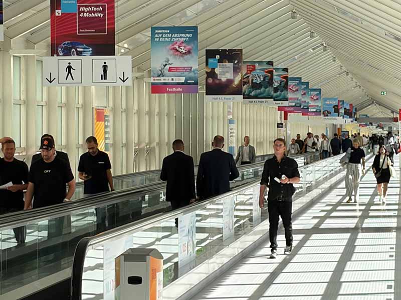 La gente camina por un pasillo del aeropuerto muy bien iluminado, con carteles, pósteres y una cinta transportadora.