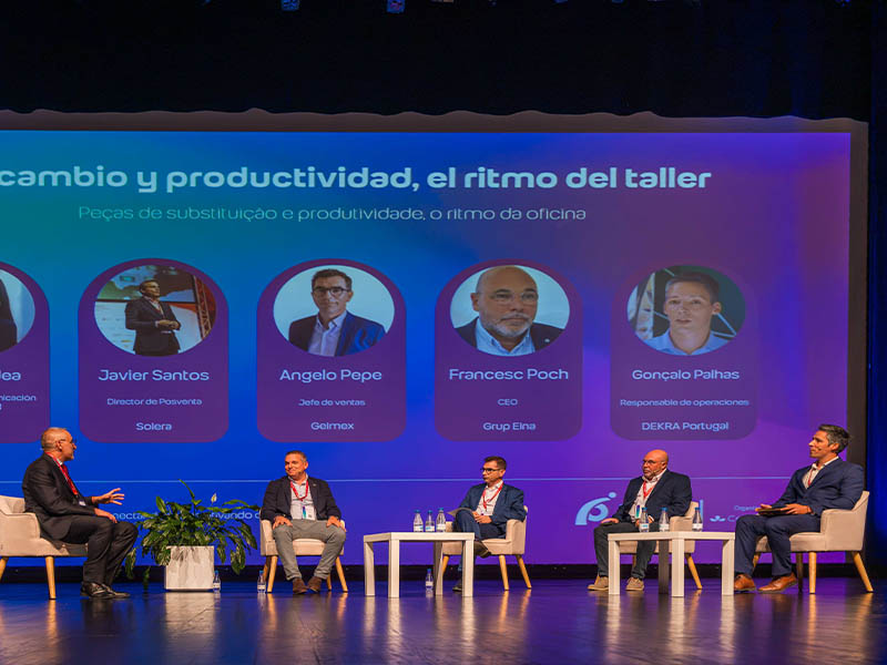 Cinco hombres vestidos con traje están sentados en el escenario, con una gran pantalla detrás de ellos en la que aparecen sus nombres y fotos.