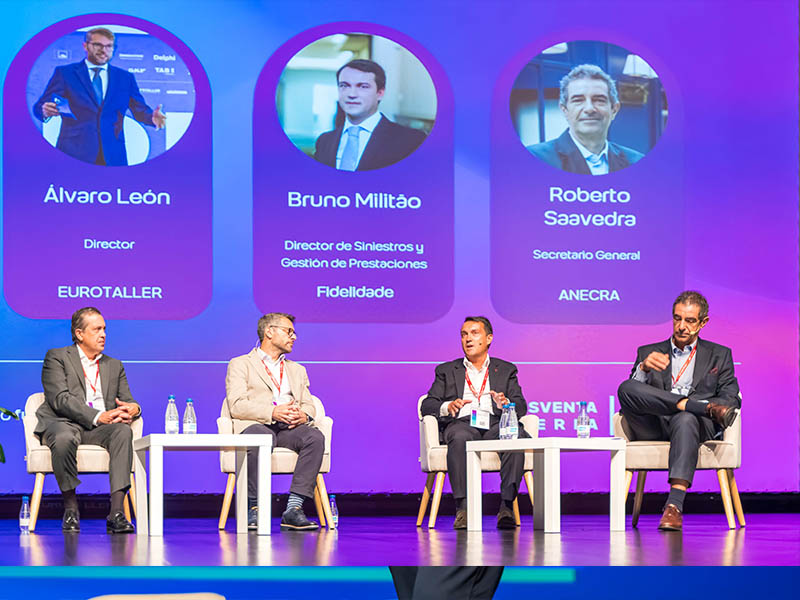 Cinco hombres están sentados en el escenario conversando, con los perfiles de tres ponentes proyectados en una pantalla situada detrás de ellos.
