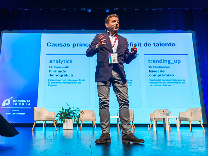 Un hombre ofrece una ponencia sobre las causas de la escasez de talento en el escenario, con una gran pantalla a sus espaldas.