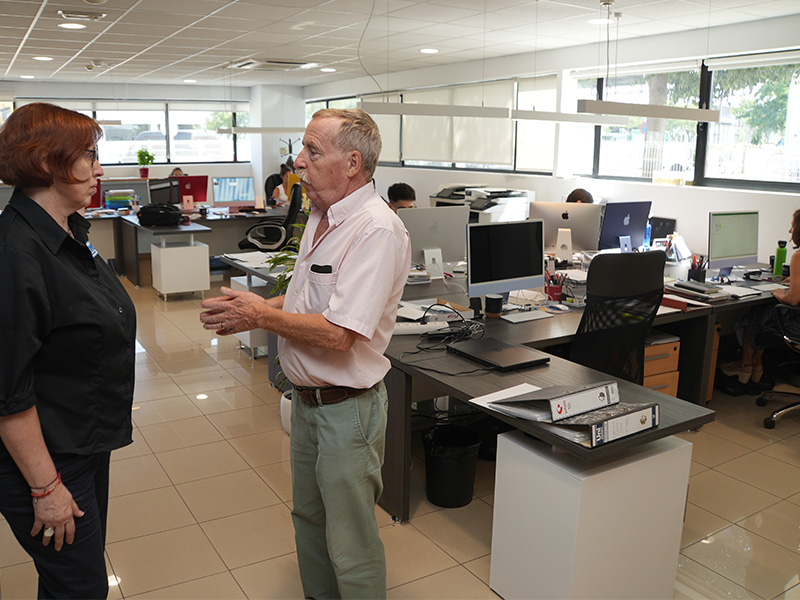 Dos compañeros de trabajo hablando sobre la transformación personal en una oficina llena de filas de escritorios.